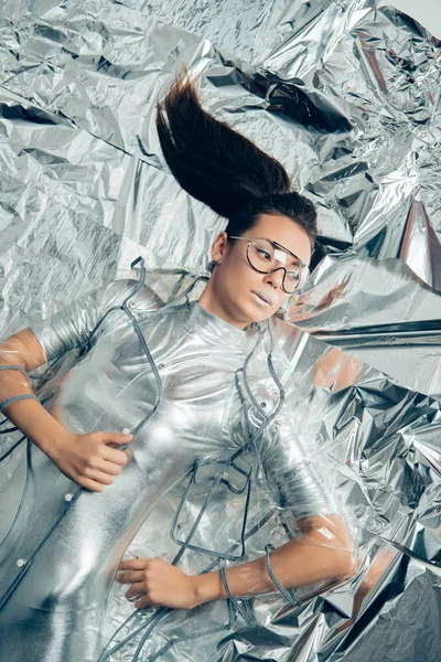 Top view of beautiful fashionable woman posing in silver bodysuit and raincoat on metallic background — Stock Photo