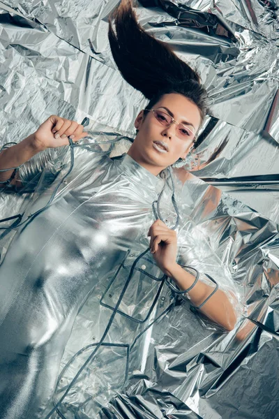 Верхний вид брюнетки модная девушка позирует в серебряном боди и дождевик на металлическом фоне — стоковое фото