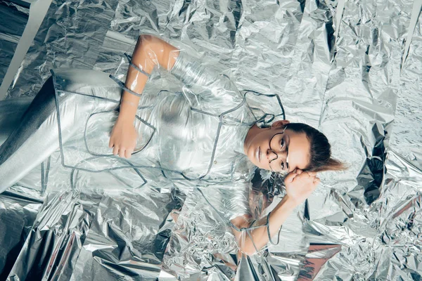 Top view of stylish beautiful girl posing in silver bodysuit and raincoat on metallic background — Stock Photo