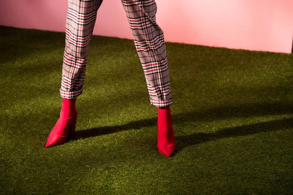 Vista parcial del modelo posando en pantalones a cuadros de moda en alfombra verde — Stock Photo