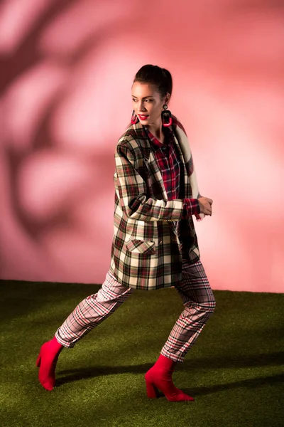 Beautiful young woman posing in checkered suit on pink background — Stock Photo