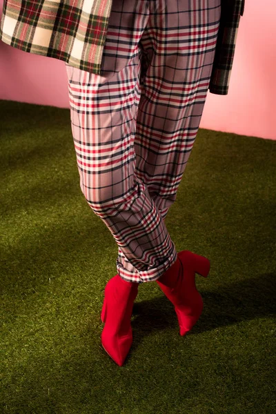 Cropped view of woman posing in fashionable checkered pants on green carpet — Stock Photo