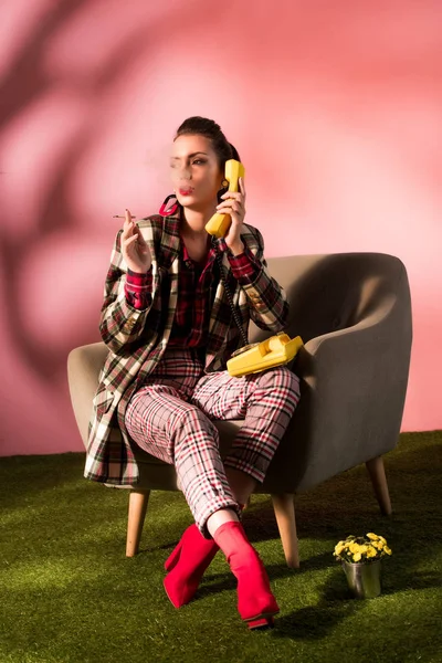 Stylische junge Frau im Sessel raucht Zigarette, während sie am Retro-Telefon spricht — Stockfoto
