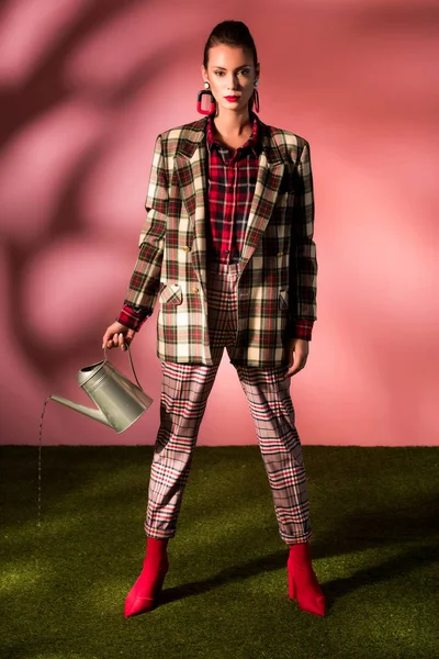 Beautiful stylish girl in autumn checkered suit posing with watering can on pink — Stock Photo