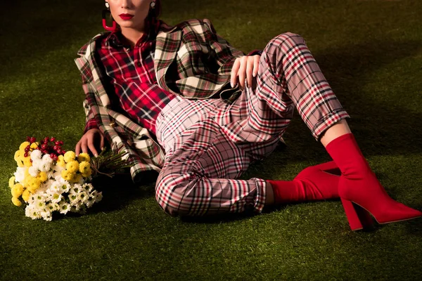 Cropped view of stylish girl in autumn checkered suit posing with bouquet of flowers on green carpet — Stock Photo