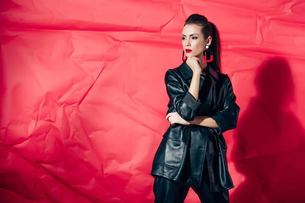 Giovane donna alla moda in posa in abito di pelle nera su sfondo rosso — Foto stock