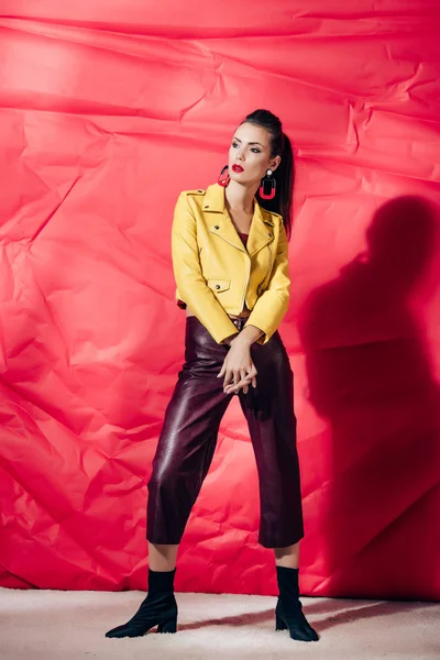 Stylisches brünettes Modell posiert in gelber Lederjacke auf rotem Hintergrund — Stockfoto