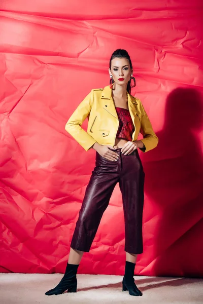 Stylish brunette model posing in yellow leather jacket on red background — Stock Photo