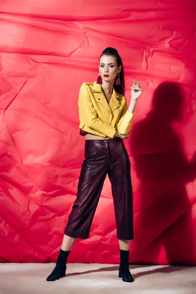 Fashionable brunette model posing in yellow leather jacket on red background — Stock Photo