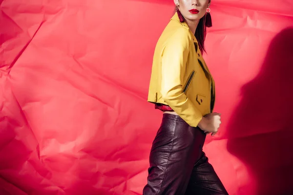 Vue recadrée du modèle à la mode posant en veste en cuir jaune sur fond rouge — Photo de stock