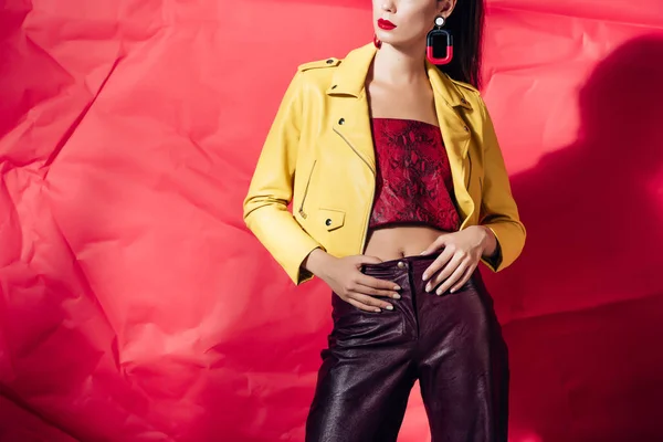 Обрезанный вид стильной женщины, позирующей в желтой кожаной куртке на красном фоне — стоковое фото