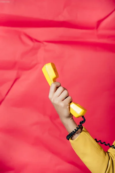 Vue recadrée de la femme tenant tube téléphonique rétro jaune sur fond rouge — Photo de stock