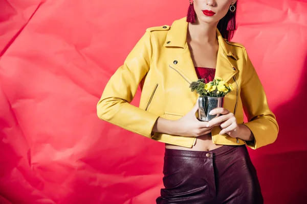 Vista recortada de la mujer en chaqueta de cuero amarillo posando con flores sobre fondo rojo - foto de stock