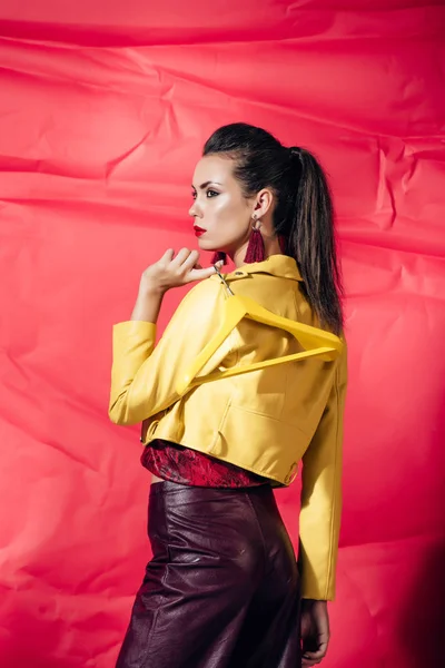 Jolie jeune femme en veste en cuir jaune posant avec cintre sur fond rouge — Photo de stock