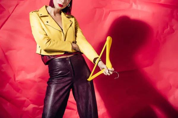 Vue recadrée du modèle en veste en cuir jaune posant avec cintre sur fond rouge — Photo de stock