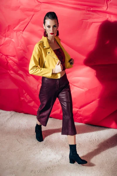 Stylish model posing in yellow leather jacket on red background for fashion shoot — Stock Photo