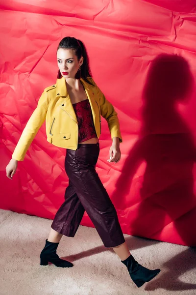 Fashionable girl posing in yellow leather jacket on red background for fashion shoot — Stock Photo