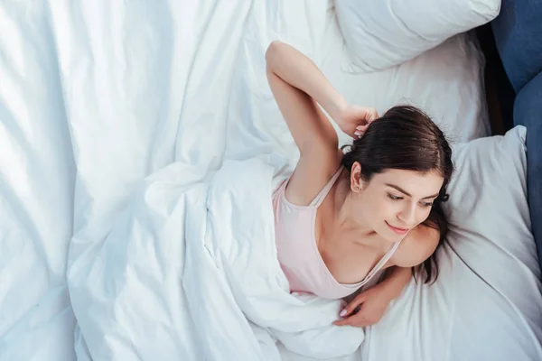 Vista de ángulo alto de la chica sonriente despertando en la cama durante el horario de la mañana en casa - foto de stock