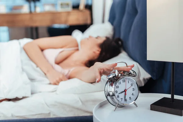 Enfoque selectivo de la chica apagando el despertador en el dormitorio durante el horario de la mañana en casa - foto de stock