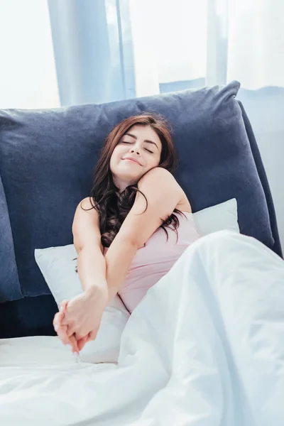 Усміхнена молода жінка тягнеться на ліжко в ранковий час вдома — стокове фото