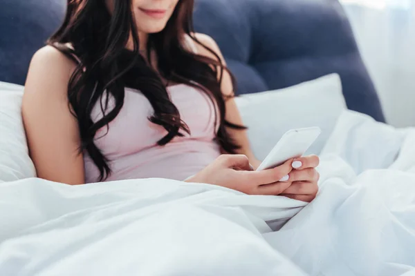 Partial view of young woman using smartphone on bed during morning time at home — Stock Photo