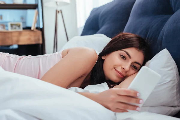 Allegra bella ragazza utilizzando smartphone sul letto durante il mattino a casa — Foto stock