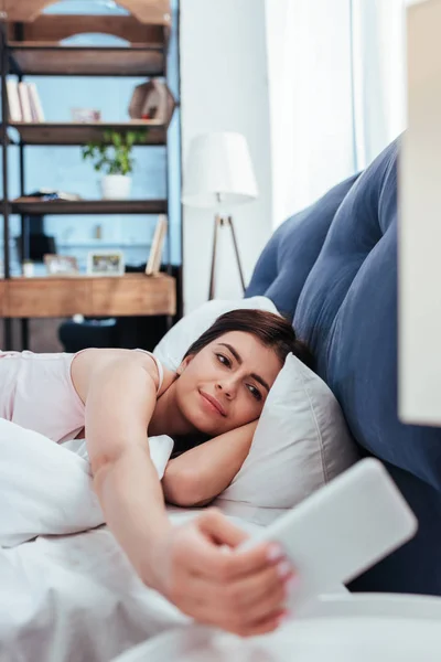 Attractive young woman using smartphone on bed during morning time at home — Stock Photo