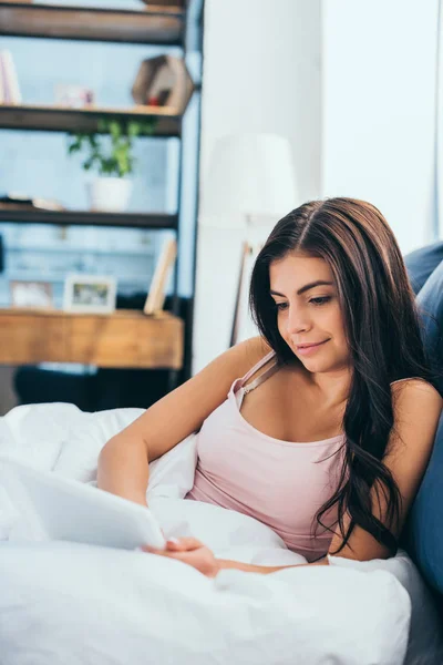 Sorridente giovane donna che utilizza tablet digitale sul letto durante il mattino a casa — Foto stock