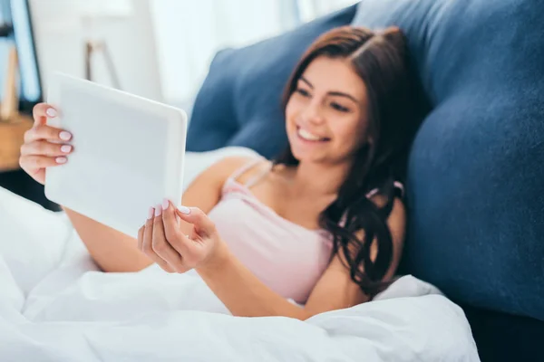Selective focus of smiling woman using digital tablet on bed during morning time at home — Stock Photo