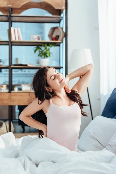 Cheerful girl stretching while sitting on bed during morning time at home — Stock Photo