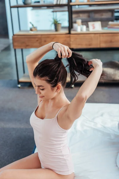 High angle view of girl collecting ponytail while sitting on bed during morning time at home — Stock Photo