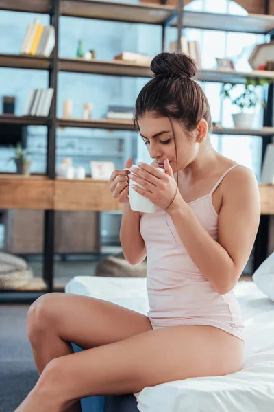 Красива молода жінка п'є чашку кави на ліжку під час ранку вдома — стокове фото