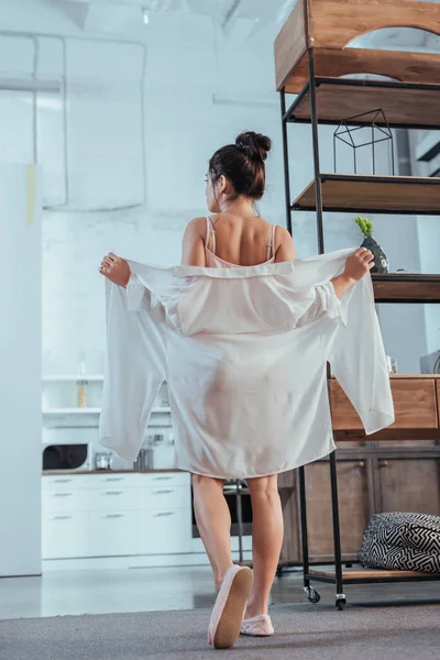 Вид сзади на молодую женщину, надевающую белую рубашку в утреннее время дома — стоковое фото