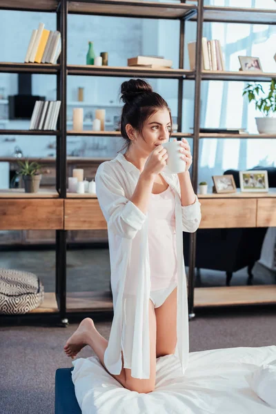 Chica bonita en camisa blanca bebiendo café durante la mañana en casa - foto de stock