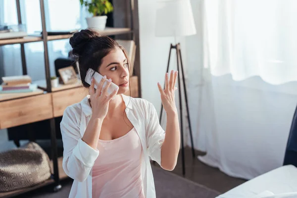 Молода жінка жестикулює рукою, розмовляючи на смартфоні в ранковий час вдома — стокове фото