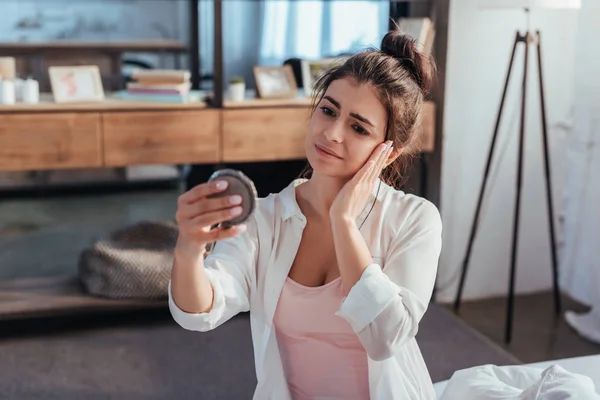 Disappointed girl looking at mirror while sitting on bed at home — Stock Photo