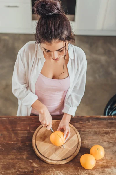 Aus der Vogelperspektive: Frau schneidet Orange mit Messer auf Holzbrett in Küche — Stockfoto