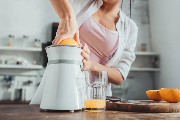 Partial view of girl making fresh orange juice with juicer at wooden table in kitchen — Stock Photo