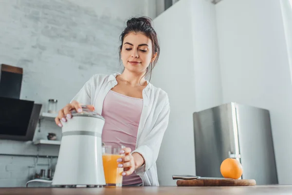 Низкий угол зрения девушка делает свежий апельсиновый сок с соковыжималкой за деревянным столом на кухне — стоковое фото
