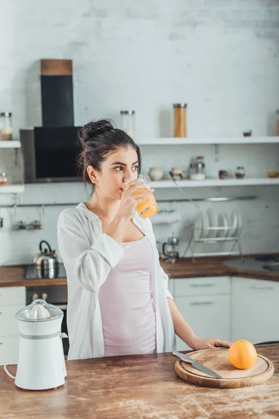Schöne junge Frau trinkt Orangensaft in der Küche zur Morgenzeit zu Hause — Stockfoto