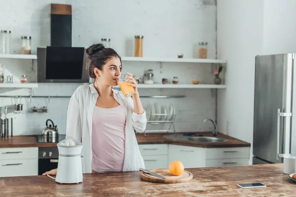 Веселая молодая женщина пьет апельсиновый сок на кухне в утреннее время дома — стоковое фото