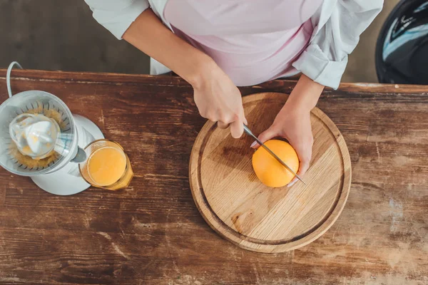 Abgeschnittenes Bild einer Frau, die in der Küche Orangen mit einem Messer auf Holzbrett schneidet — Stockfoto