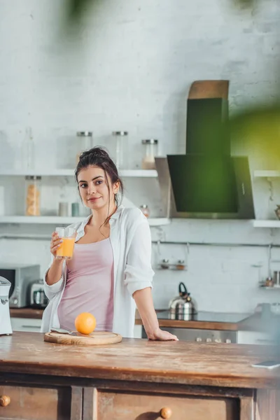 Selektiver Fokus der jungen Frau, die morgens zu Hause eine Tasse mit Orangensaft in der Küche hält — Stockfoto