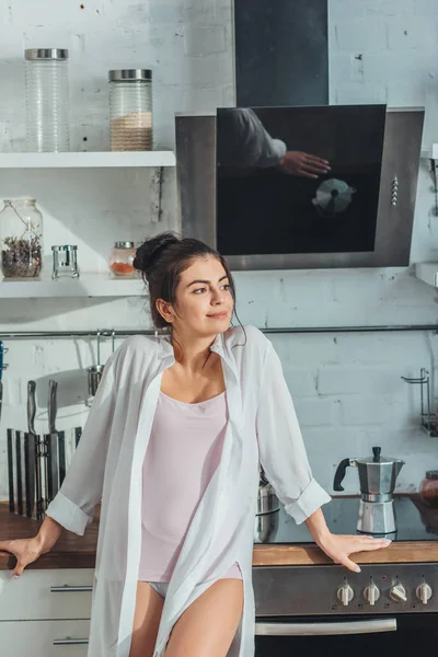 Приваблива молода жінка, дивлячись геть, стоячи на кухні вдома — стокове фото