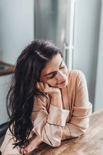 Freudig schöne junge Frau sitzt an hölzerner Tischplatte in Küche zu Hause — Stockfoto