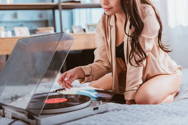 Partial view of young woman turning on vinyl audio player while sitting on bed at home — Stock Photo