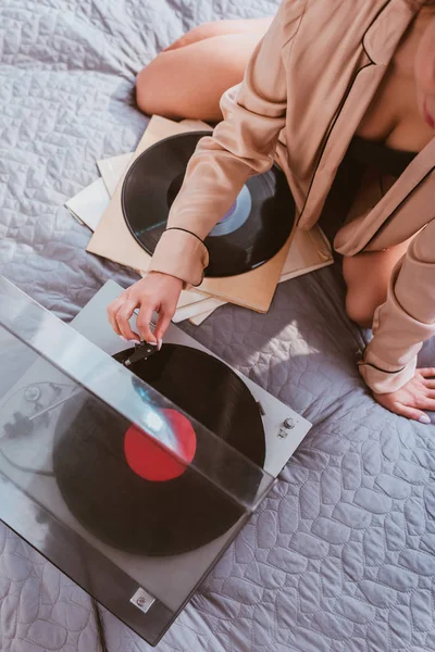 Partial view of young woman turning on vinyl audio player while sitting on bed at home — Stock Photo