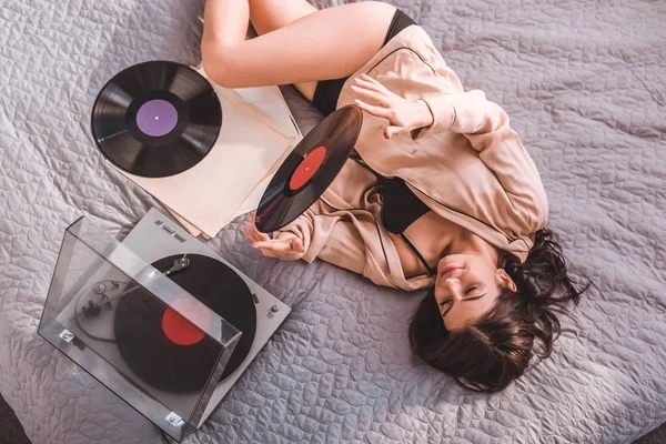 Ansicht einer Frau, die auf dem Bett liegt und zu Hause Vinyl-Audio-Player hört — Stockfoto