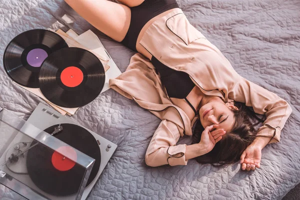 Blick aus der Vogelperspektive auf eine junge, fröhliche Frau, die zu Hause auf dem Bett liegt und Vinyl-Audio-Player hört — Stockfoto