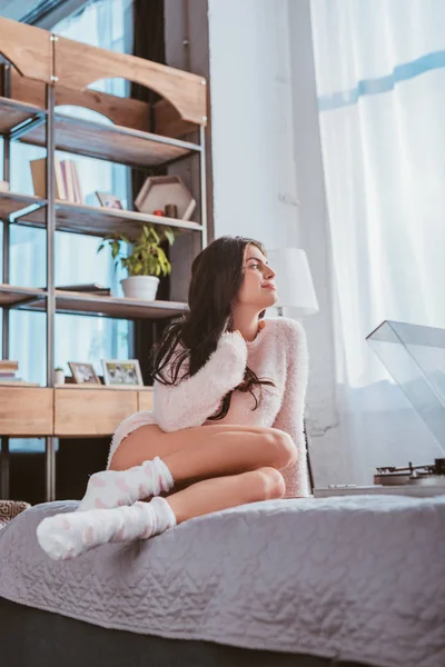 Счастливая девушка сидит на кровати и слушает дома виниловый аудиоплеер — стоковое фото